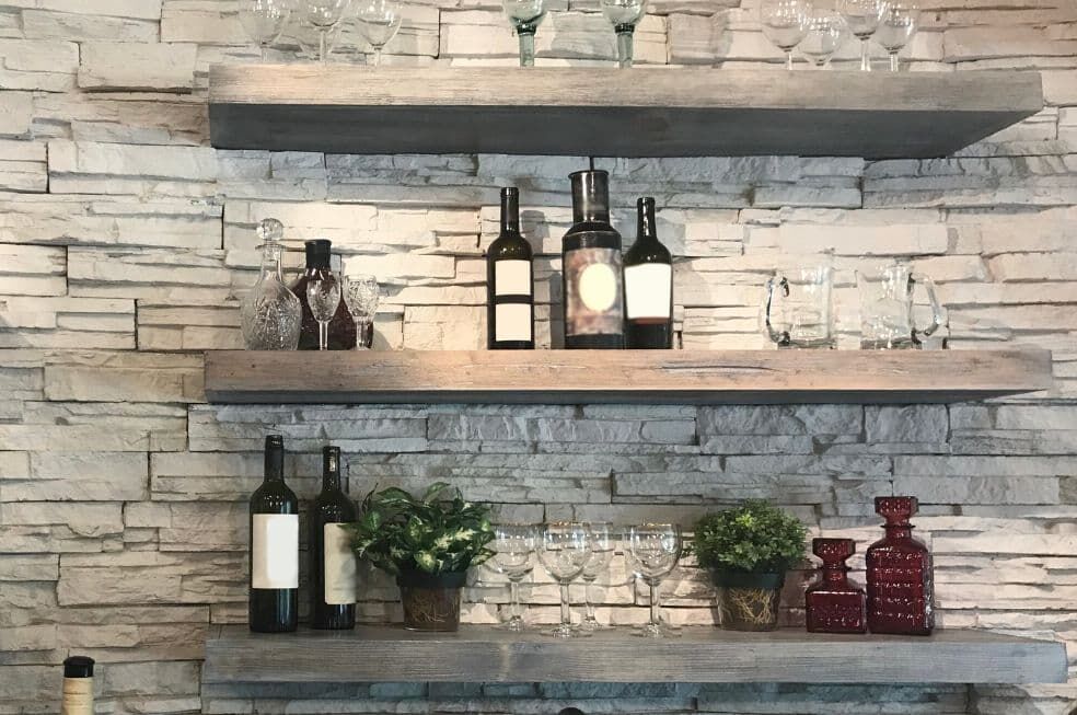 szare, grube półki ścienne do kuchni na ścianie z jasnego kamienia z butelkami wina i kieliszkami