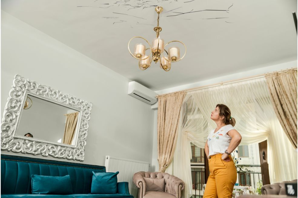 kobieta oglądająca popękany sufit koło lampy wiszącej w pokoju