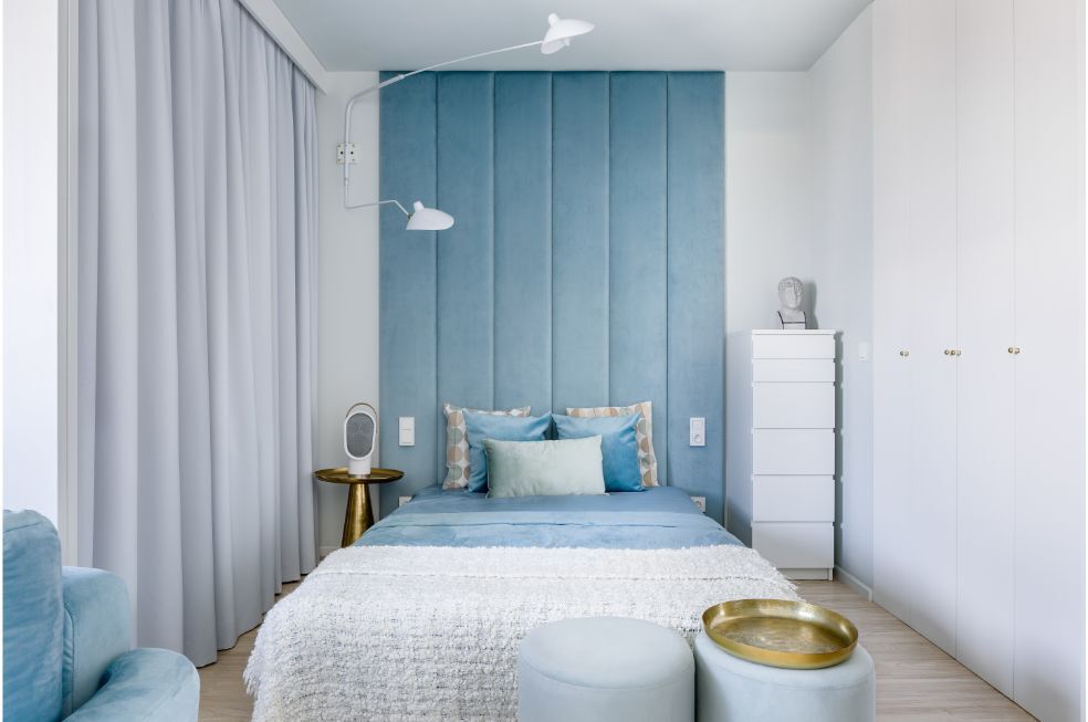 sypialnia z niebieskimi, tapicerowanymi panelami na ścianie za łóżkiem