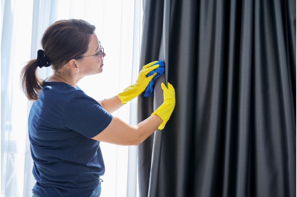 Sprzątanie domu, kobieta w rękawiczkach ze szmatką do czyszczenia zasłon