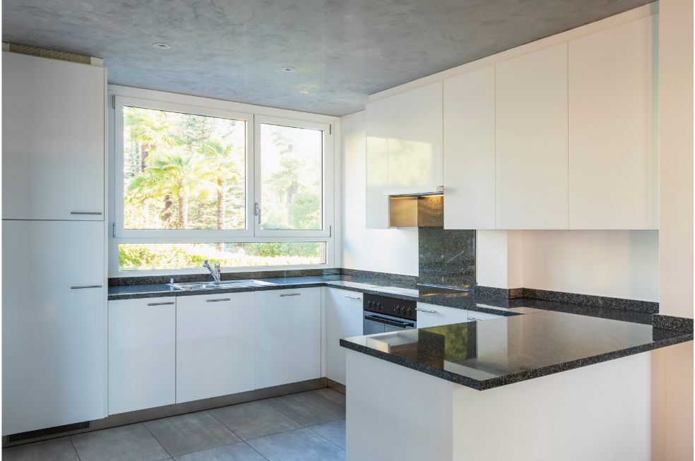 biała kuchnia zabudowana z dużym oknem i czarnym marmurowym blatem