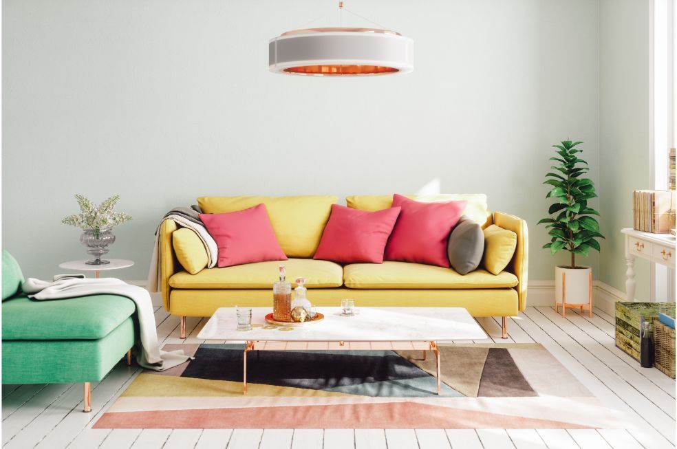 żółta sofa z czerwonymi poduszkami i zielony fotel w pomieszczeniu z białym stołem i miedzianą okrągłą lampą