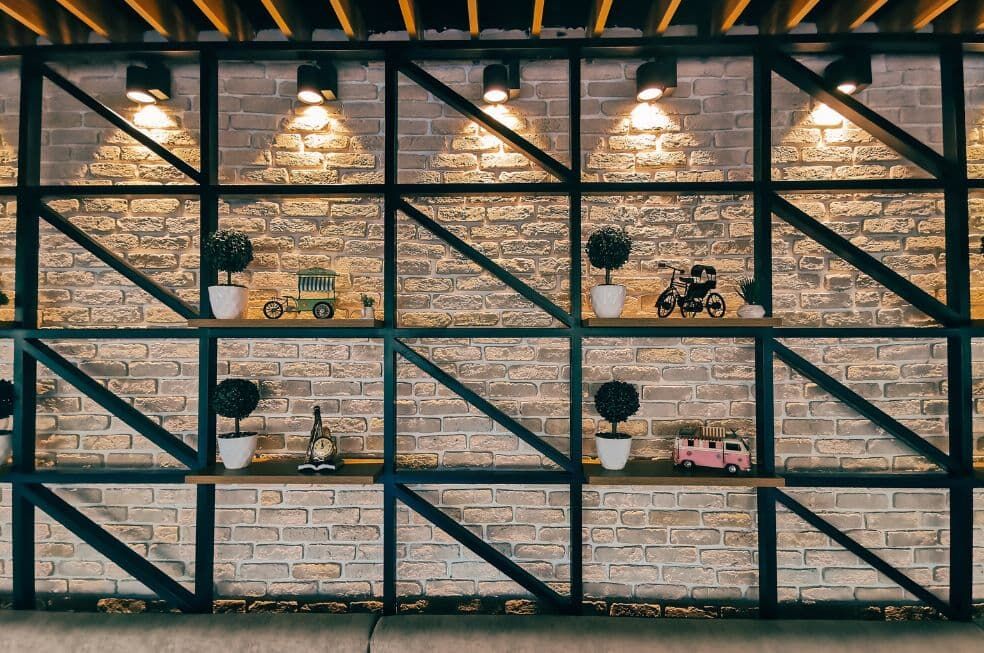 czarne półki na ścianie z cegły podświetlone od góry