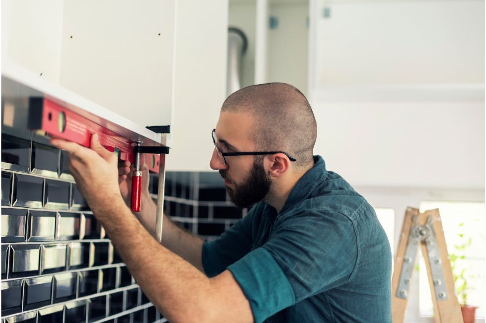 mężczyzna montujący półkę w kuchni na czarnej ścianie z płytek
