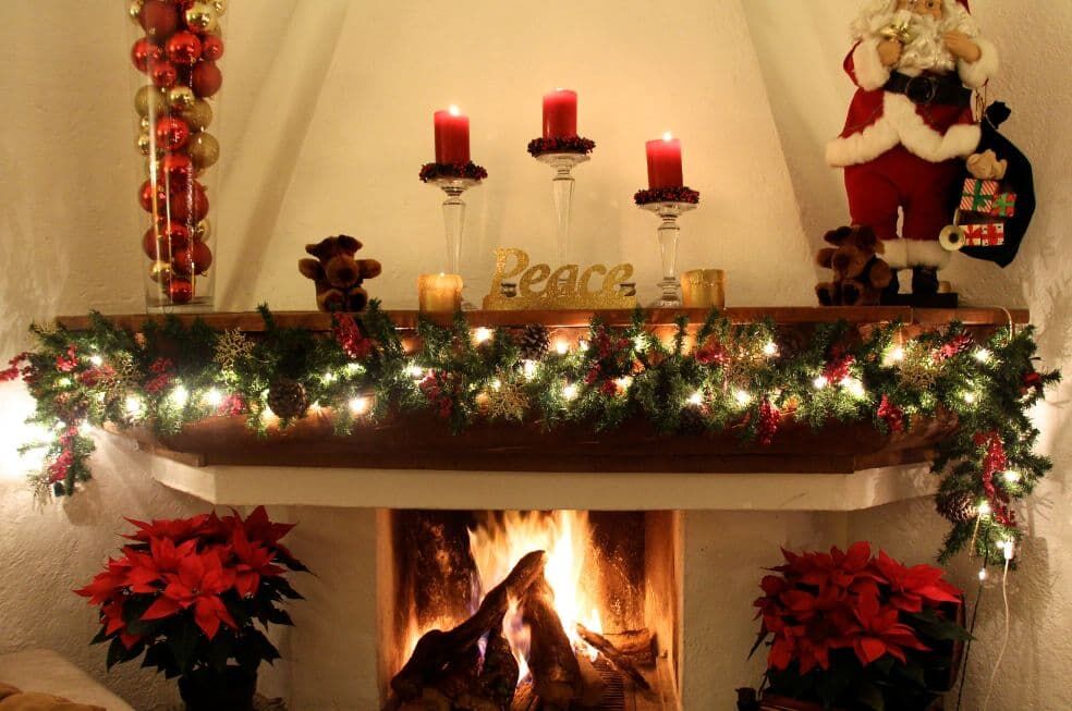 palące się drzewo w kominku ozdobionym girlandą i świątecznymi lampkami, z czerwonymi kwiatami gwiazdy betlejemskiej