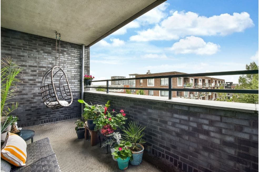 zabudowany balkon z ciemnych cegieł z wiszącym fotelem ozdobiony kwiatami w doniczkach