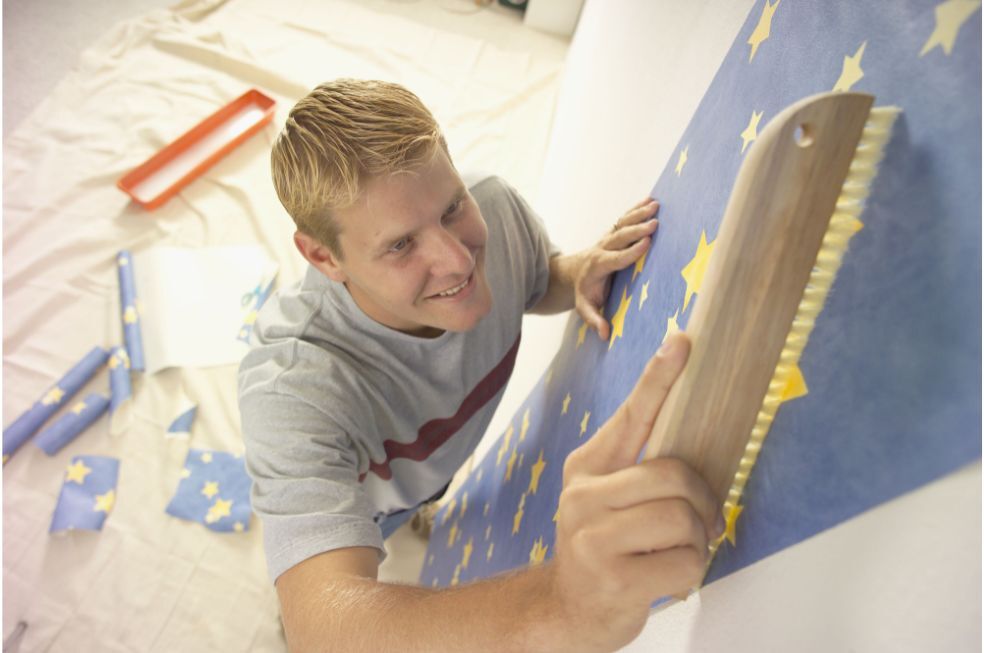 mężczyzna kładący niebieską tapetę w gwiazdki na ścianie