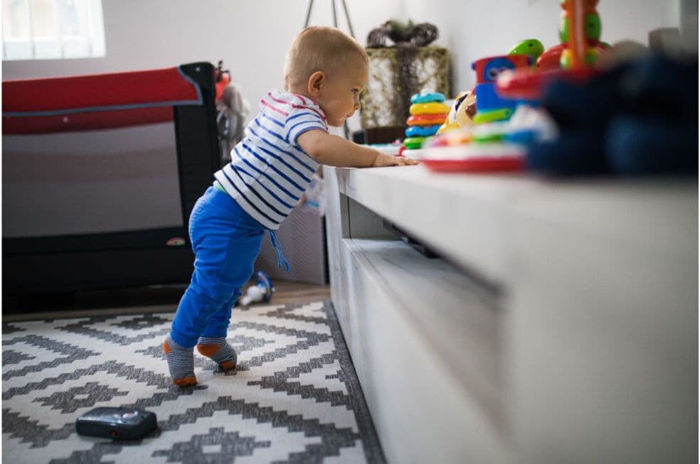 małe dziecko stojące przy niskiej szafce w salonie