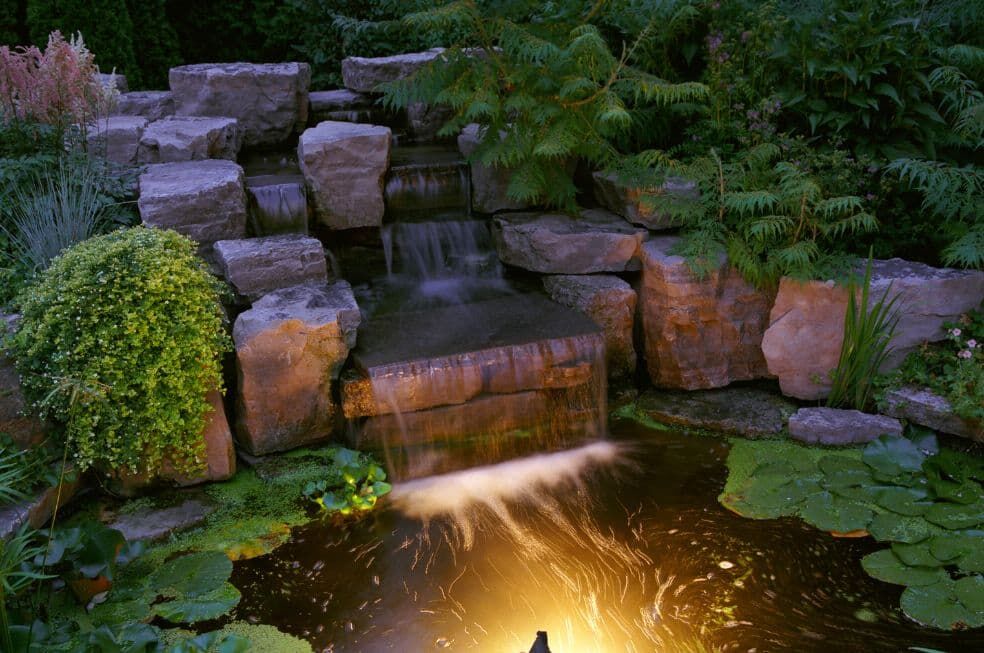 podświetlony wodospad na oczku wodnym w ogrodzie nocą