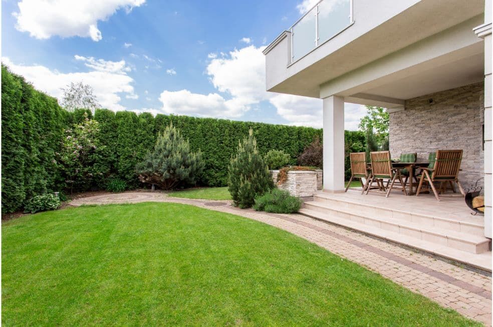 kawałek ogródka ogrodzonego tujami z trawnikiem i tarasem przy domu