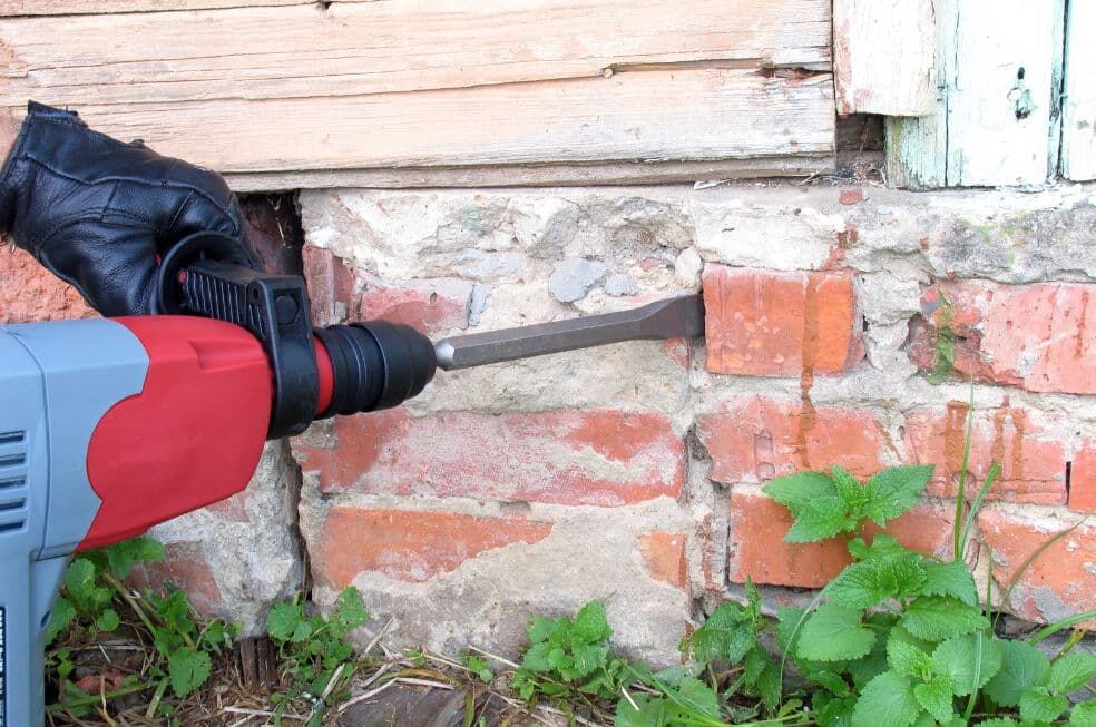 mężczyzna burzący murek z cegieł za pomocą wiertarki