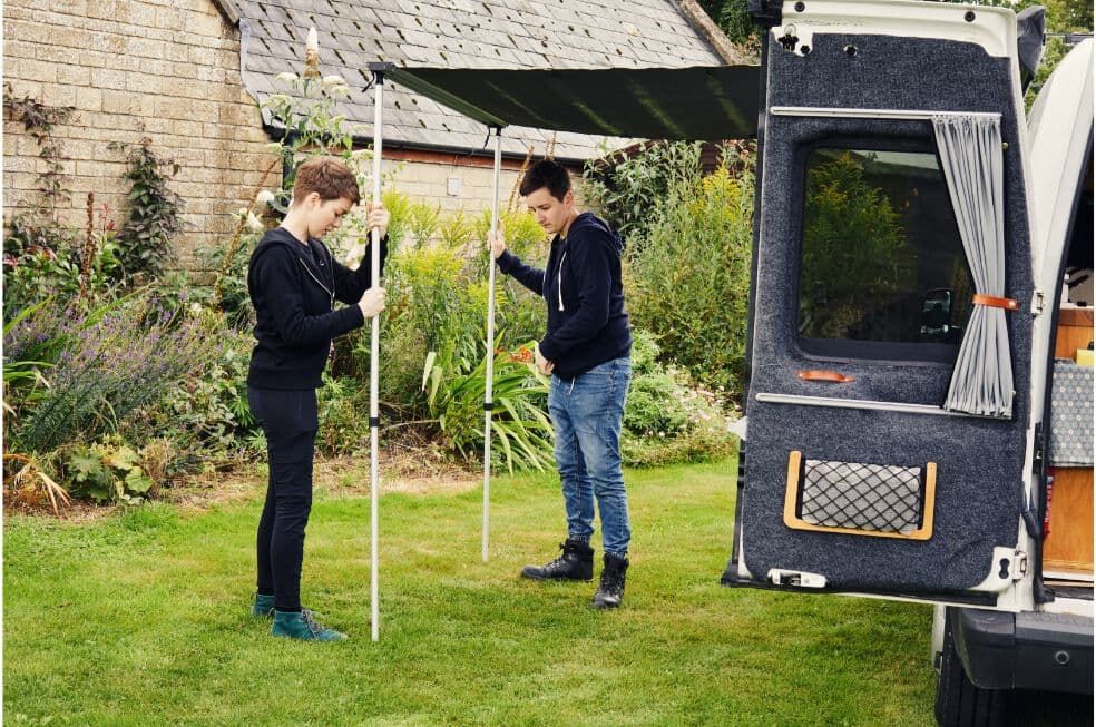 chłopak i dziewczyna rozkładają daszek przy kamperze